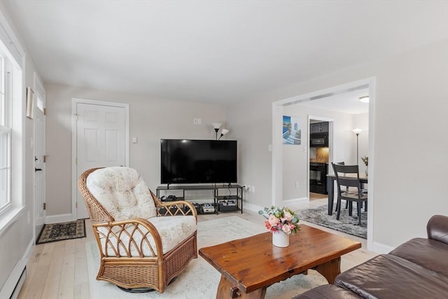 living area featuring a baseboard heating unit, baseboards, plenty of natural light, and light wood finished floors