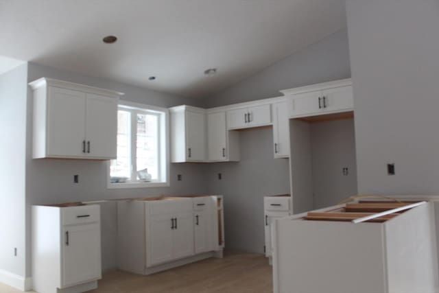 kitchen featuring lofted ceiling, light wood-type flooring, white cabinets, and a center island