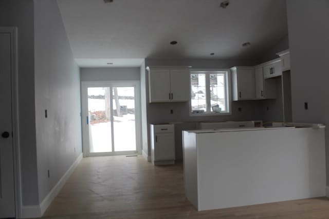 kitchen featuring baseboards, a kitchen island, light wood-style flooring, and white cabinets