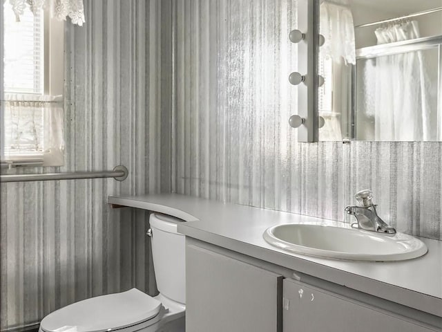 bathroom featuring wallpapered walls, toilet, vanity, and curtained shower
