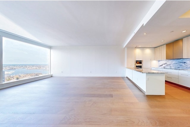 kitchen with light hardwood / wood-style floors, white cabinetry, light stone countertops, and tasteful backsplash