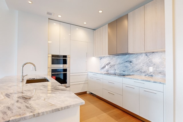 kitchen featuring light stone counters, sink, kitchen peninsula, black electric cooktop, and stainless steel double oven