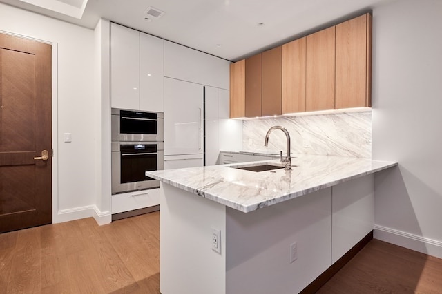 kitchen with light wood-type flooring, light stone counters, sink, white cabinetry, and double oven