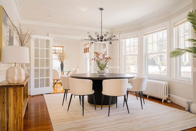 dining room with hardwood / wood-style flooring, crown molding, radiator, and a notable chandelier