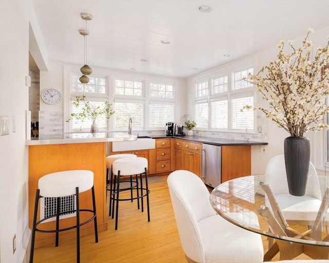 kitchen featuring pendant lighting, sink, fridge, kitchen peninsula, and light hardwood / wood-style flooring