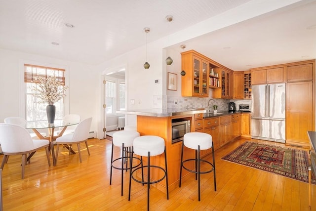 kitchen featuring pendant lighting, a breakfast bar area, backsplash, stainless steel appliances, and light hardwood / wood-style flooring