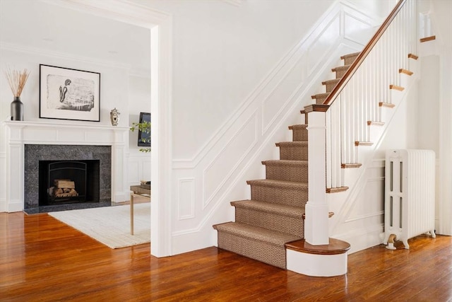 stairway featuring hardwood / wood-style flooring, radiator heating unit, ornamental molding, and a high end fireplace