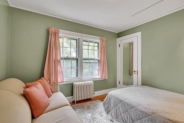 bedroom with ornamental molding, radiator heating unit, wood finished floors, and baseboards