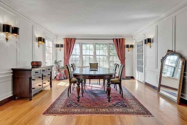 dining space featuring crown molding, a decorative wall, and light wood-style flooring