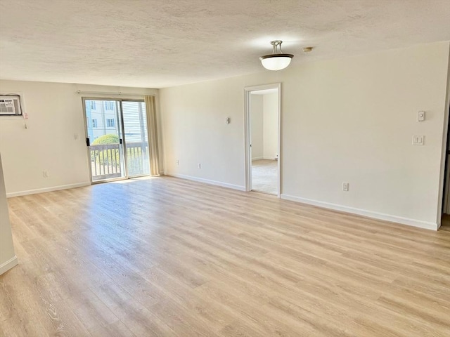 unfurnished room with light wood-type flooring, a wall mounted AC, baseboards, and a textured ceiling