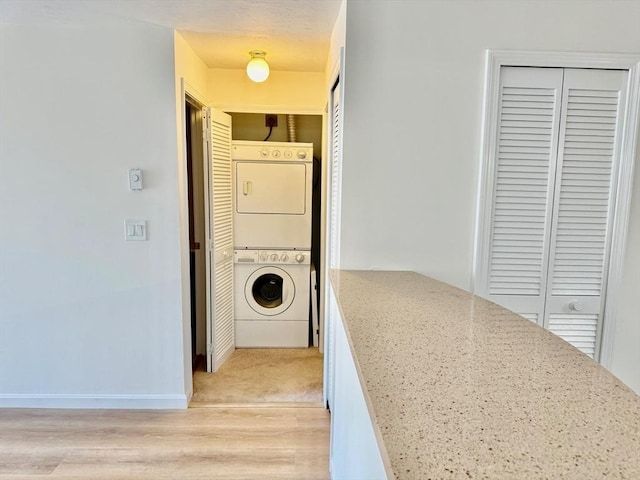 laundry area featuring baseboards, stacked washer and dryer, laundry area, and light wood-type flooring