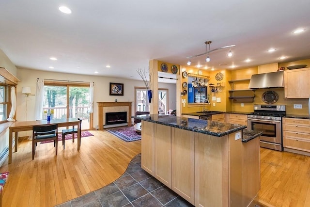 18 W Shore Dr, Goshen, MA 01032 - kitchen featuring stainless steel gas stove, wall chimney range hood, a sink, a fireplace with flush hearth, and dark stone countertops