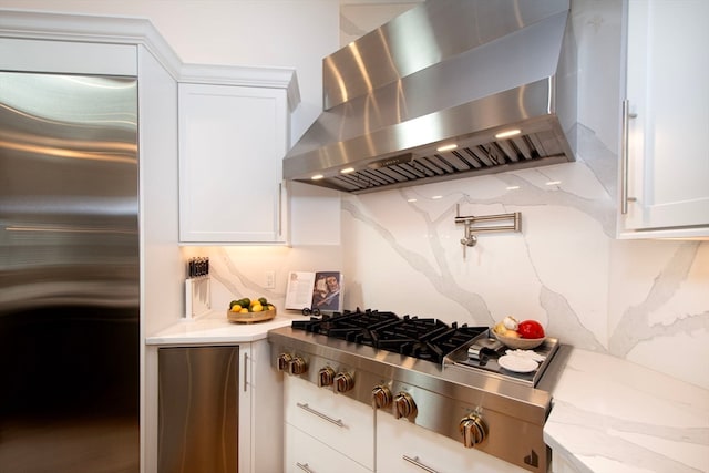 kitchen with wall chimney exhaust hood, white cabinetry, stainless steel appliances, and backsplash