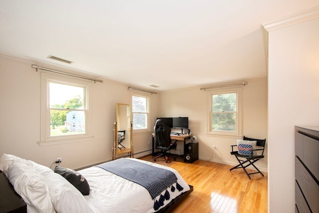 bedroom featuring ornamental molding, light wood-type flooring, a baseboard heating unit, and multiple windows