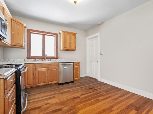 kitchen featuring baseboards, light stone countertops, dark wood finished floors, appliances with stainless steel finishes, and a sink