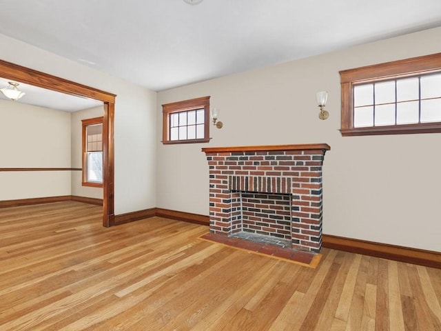 unfurnished living room with baseboards, a brick fireplace, and wood finished floors