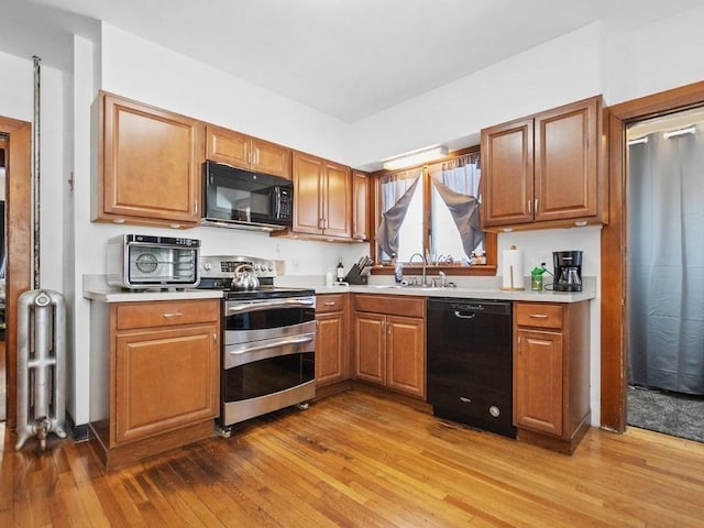 kitchen with light wood-type flooring, black appliances, light countertops, and a sink