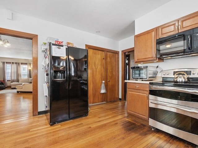 kitchen with light wood-style floors, black appliances, brown cabinetry, and light countertops