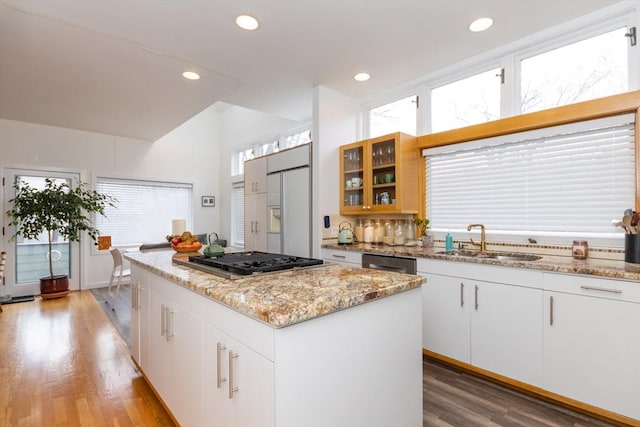 kitchen with light stone countertops, a sink, stainless steel appliances, light wood-type flooring, and a kitchen island