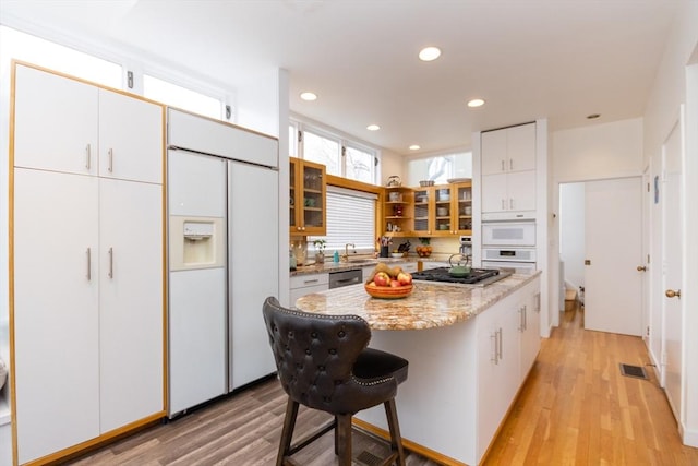 kitchen with glass insert cabinets, appliances with stainless steel finishes, visible vents, a kitchen island, and light wood finished floors
