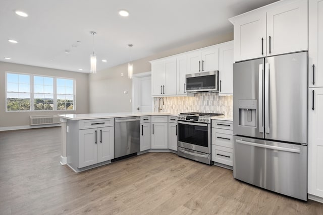 kitchen with appliances with stainless steel finishes, white cabinetry, kitchen peninsula, pendant lighting, and light wood-type flooring