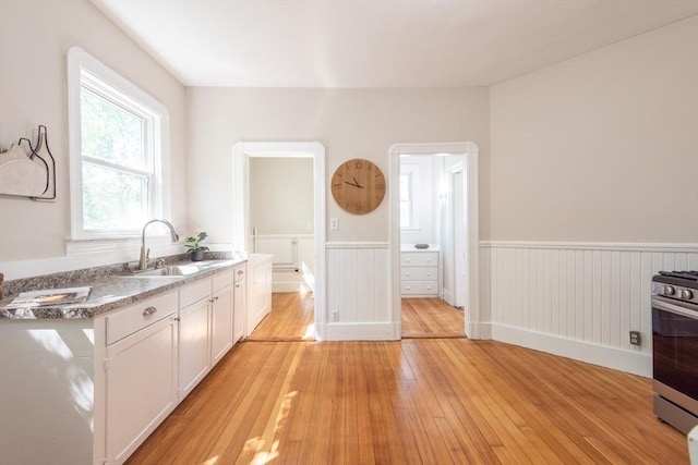 1690 Centre St Unit 2, Boston, MA 02132 - kitchen with a sink, stainless steel gas stove, a wainscoted wall, light wood finished floors, and white cabinetry