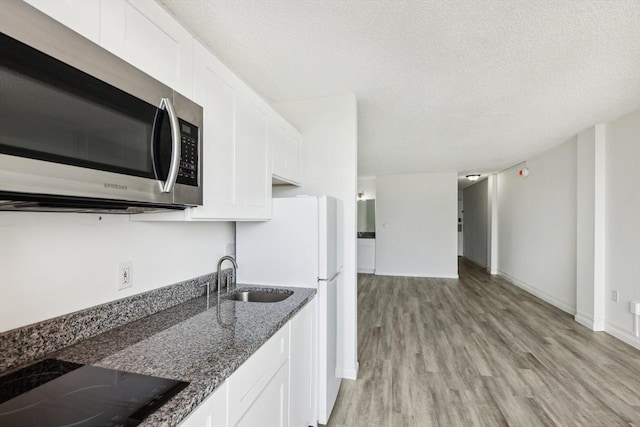 935 S Atlantic Unit 302, Daytona Beach, FL 32118 - kitchen with stainless steel microwave, black electric cooktop, light wood-style floors, white cabinets, and dark stone counters