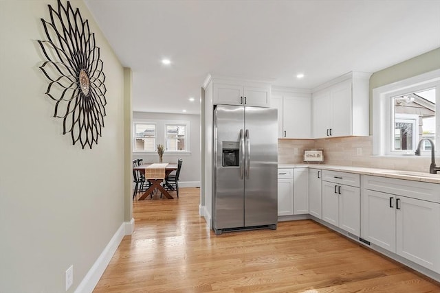 kitchen with decorative backsplash, stainless steel refrigerator with ice dispenser, a sink, light countertops, and light wood finished floors