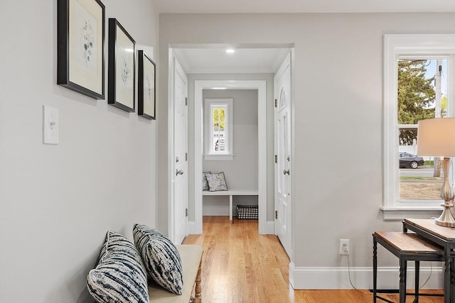 hall featuring light wood-style floors, baseboards, ornamental molding, and a wealth of natural light