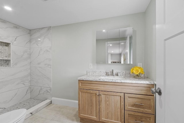 full bath featuring a tile shower, tile patterned flooring, vanity, toilet, and baseboards