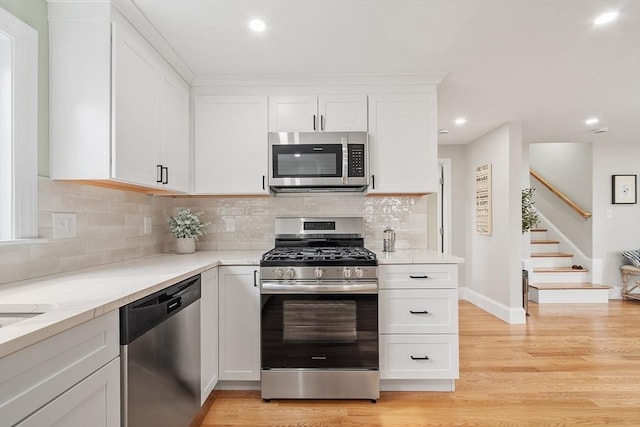 kitchen with light stone countertops, stainless steel appliances, white cabinetry, decorative backsplash, and light wood-type flooring