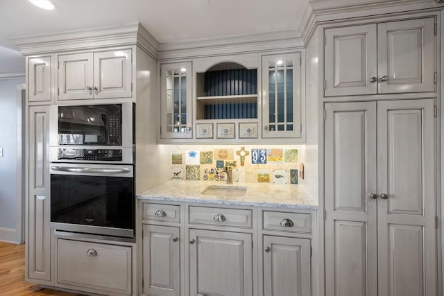 kitchen with sink, light hardwood / wood-style flooring, light stone countertops, decorative backsplash, and stainless steel oven