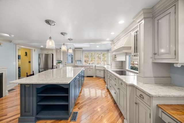 kitchen with a center island, stainless steel fridge, pendant lighting, black electric stovetop, and light stone countertops