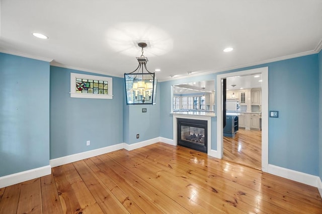 unfurnished living room with an inviting chandelier, ornamental molding, and light hardwood / wood-style flooring