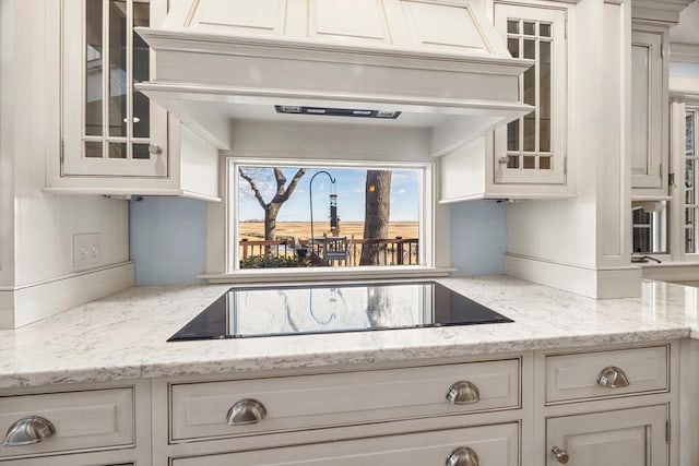 kitchen with black electric cooktop, white cabinetry, premium range hood, and light stone counters