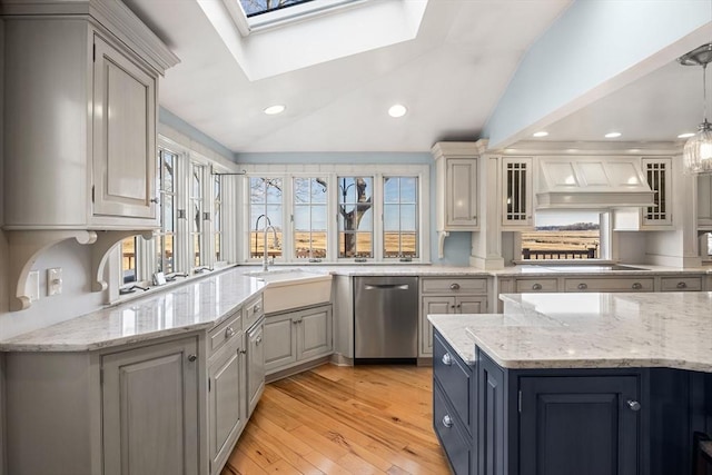 kitchen with premium range hood, lofted ceiling with skylight, sink, decorative light fixtures, and stainless steel dishwasher