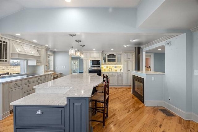 kitchen with hanging light fixtures, a spacious island, black appliances, a kitchen bar, and decorative backsplash