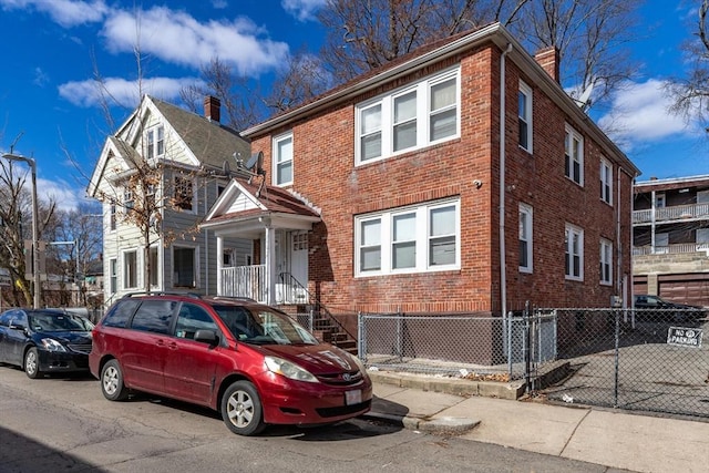 view of front facade with brick siding, a chimney, and fence