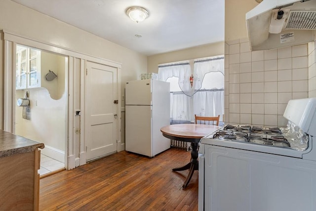 kitchen with white appliances, under cabinet range hood, decorative backsplash, and wood finished floors