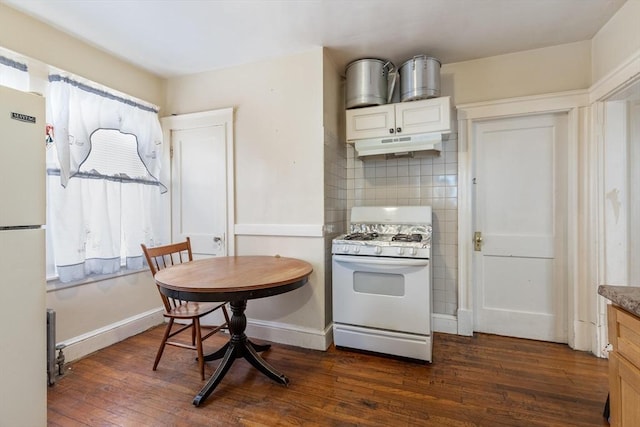 kitchen with tasteful backsplash, dark wood-type flooring, white appliances, under cabinet range hood, and baseboards