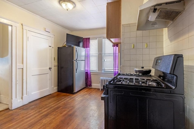 kitchen with radiator, wood finished floors, freestanding refrigerator, backsplash, and gas stove