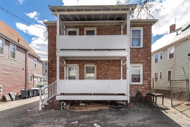 multi unit property with a balcony, covered porch, and brick siding