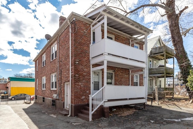 view of side of property featuring a balcony, a chimney, and brick siding