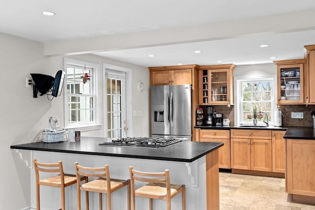 kitchen with stainless steel appliances, a sink, decorative backsplash, dark countertops, and glass insert cabinets