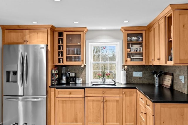 kitchen with dark countertops, a sink, glass insert cabinets, and stainless steel fridge with ice dispenser