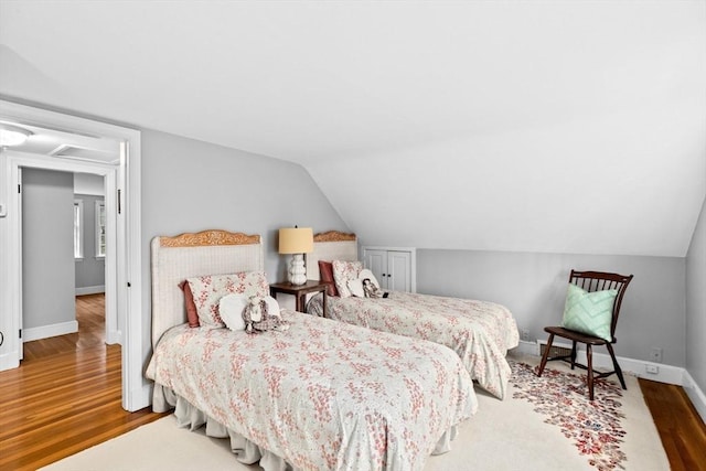 bedroom with baseboards, vaulted ceiling, and wood finished floors