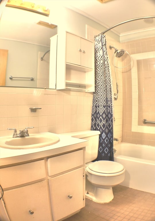 bathroom with toilet, ornamental molding, shower / tub combo with curtain, vanity, and tile walls