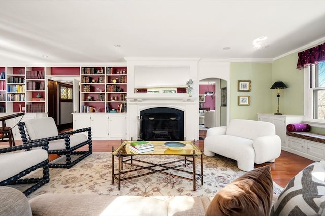 living area featuring crown molding, a fireplace, arched walkways, and wood finished floors