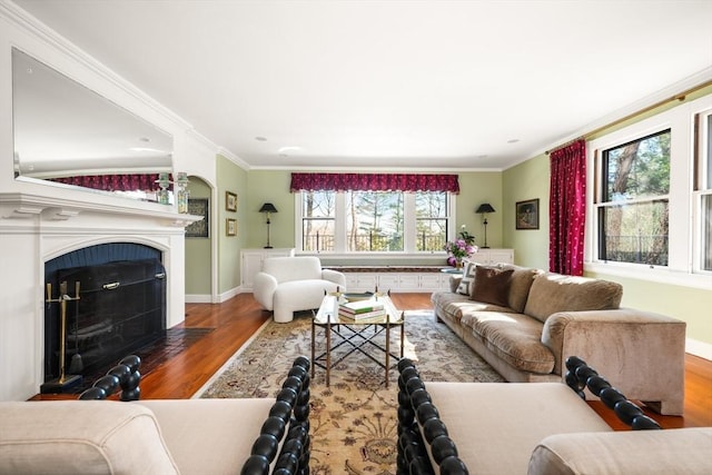 living area featuring baseboards, a fireplace with flush hearth, ornamental molding, and wood finished floors