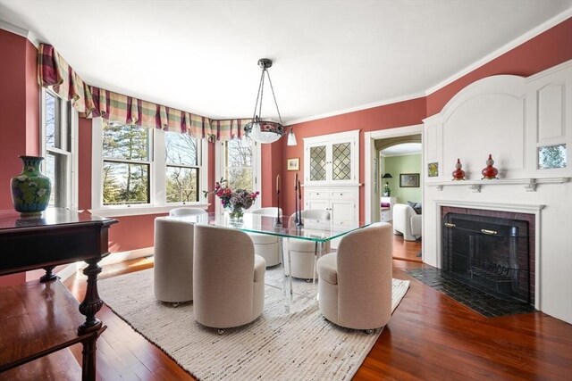 dining area with a fireplace with flush hearth, ornamental molding, arched walkways, and wood finished floors